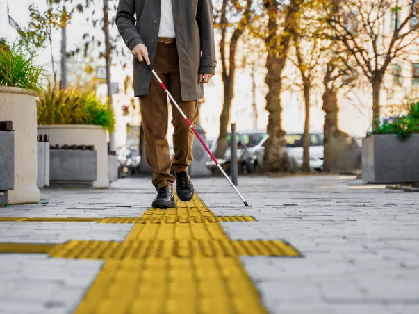 Une personne malvoyante marche sur un trottoir en suivant une bande tactile jaune avec une canne blanche à Varennes en Indre-et-Loire 37