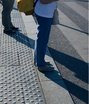 Deux personnes sur un trottoir texturé attendent au bord d'une route ombragée à Varennes en Indre-et-Loire 37