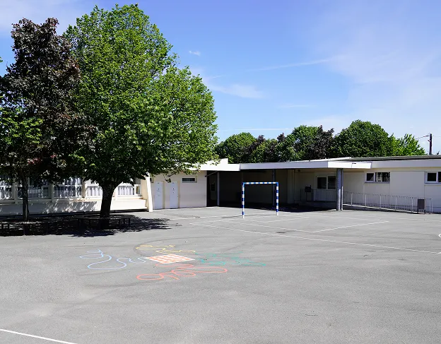 Cour d'école ensoleillée avec un grand arbre, un but de foot et des bâtiments blancs à Varennes en Indre-et-Loire 37